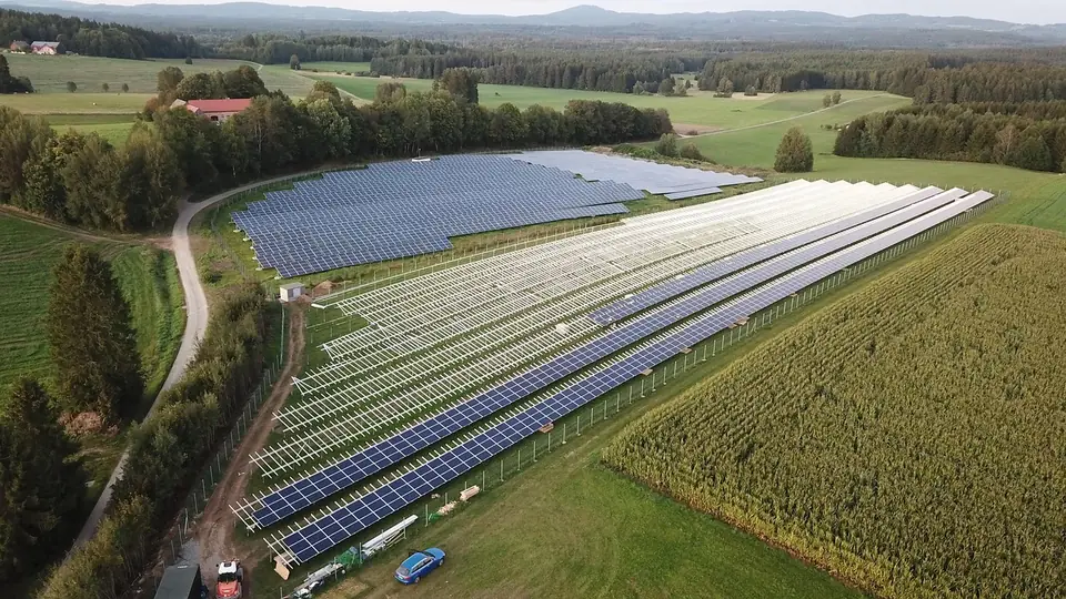 Vue aérienne de rangées de panneaux photovoltaïques installés entre des champs et une forêt