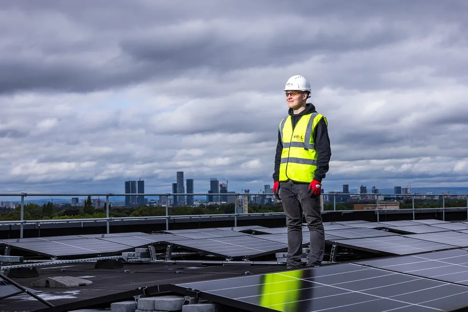 Technicien en gilet de sécurité et casque blanc debout sur un toit plat couvert de panneaux solaires
