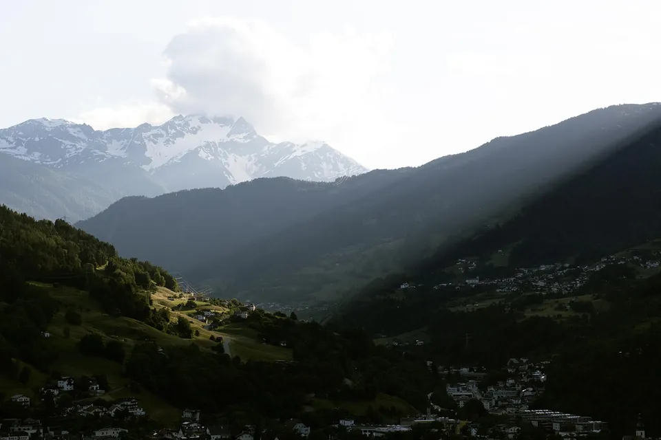 Vallée alpine boisée avec un village au pied de sommets enneigés