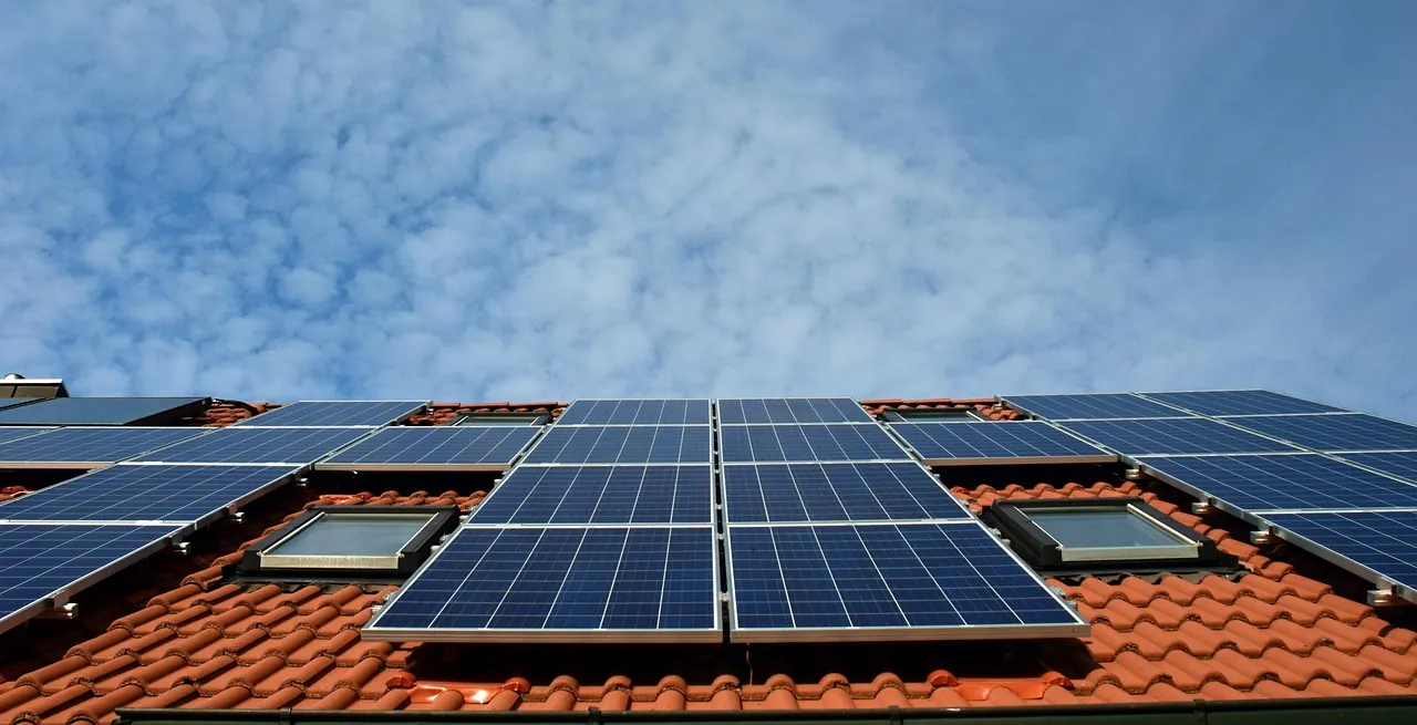 Panneaux solaires posés sur un toit de tuiles rouges, sous un ciel bleu nuageux